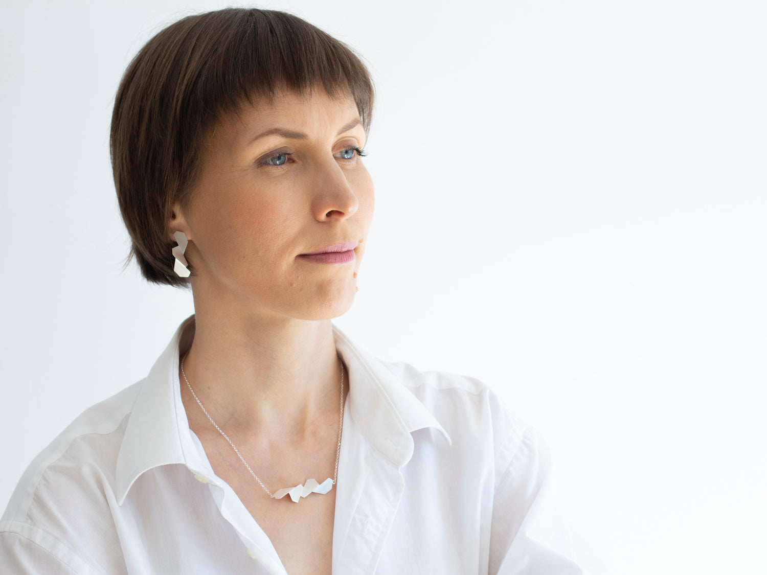 A model wearing silver jewelry - stud earrings and geometric necklace