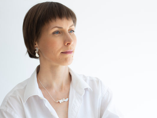 A woman in white shirt wearing geometric folded sterling silver earrings and geometric sterling silver pendant neklacee