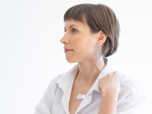 A woman with a white shirt wearing geometric statement earrings in sterling silver.